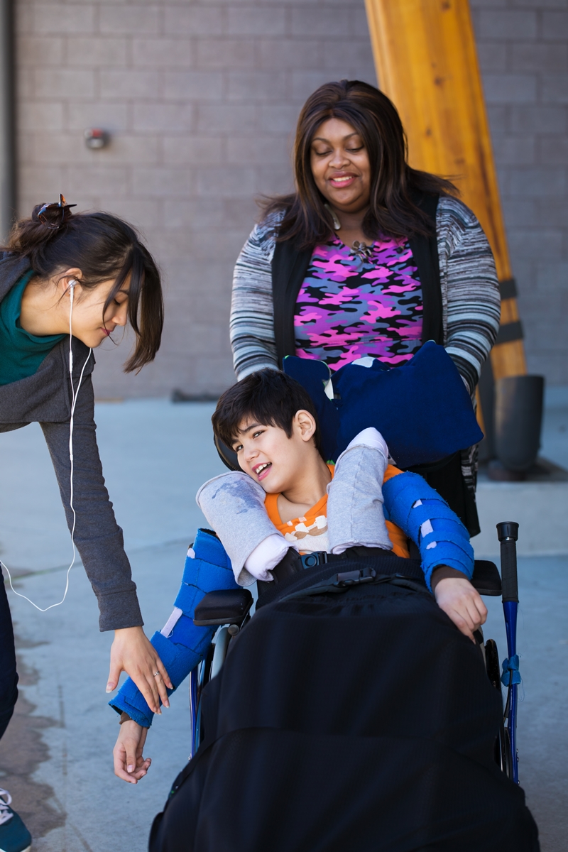 diverse caregivers assist disabled child in wheelchair